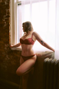 a woman in a red lingerie leaning against a window